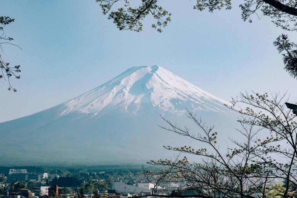 Mount Fuji viewed from a distance with a clear blue sky and foliage in the foreground, captured in our Asia Travel Guide.