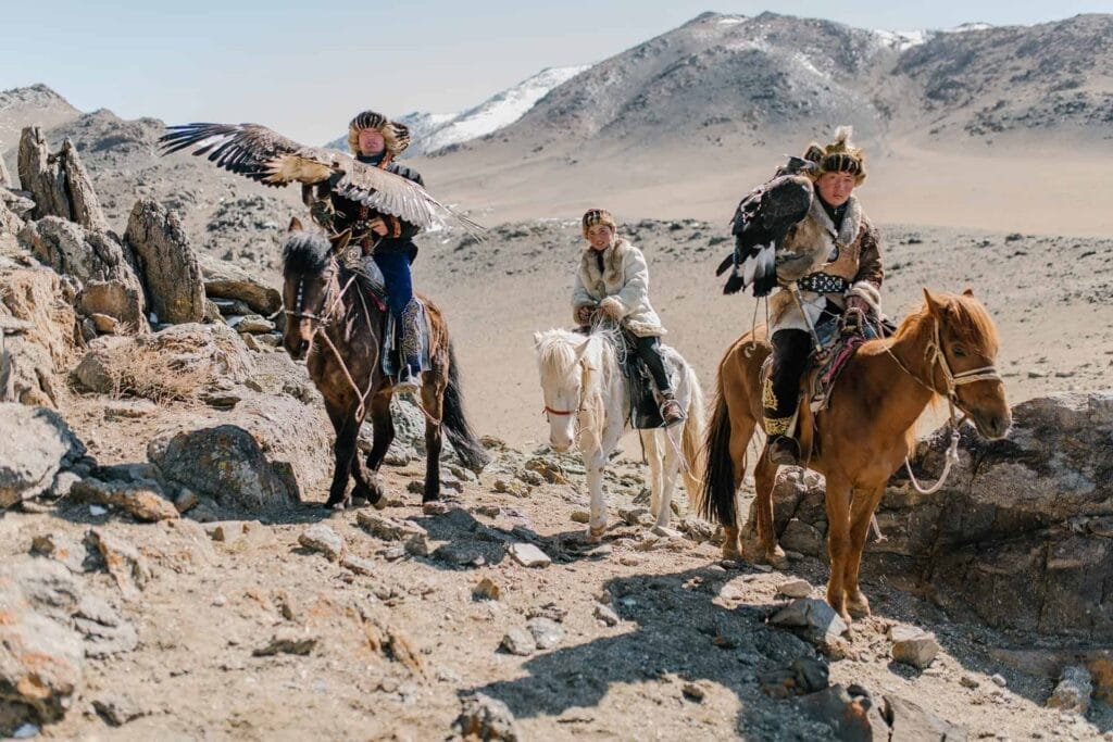 Three eagle hunters mounted on horses in a mountainous landscape, experiencing the perfect weekend in Asia.