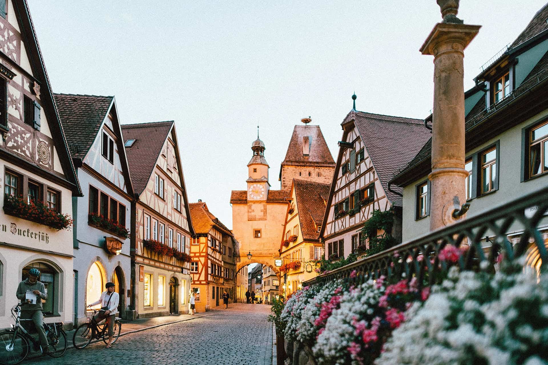Twilight over a charming European old town street with traditional half-timbered houses and a clock tower in the background, captured in the "Train Travel Guide" for beginners.
